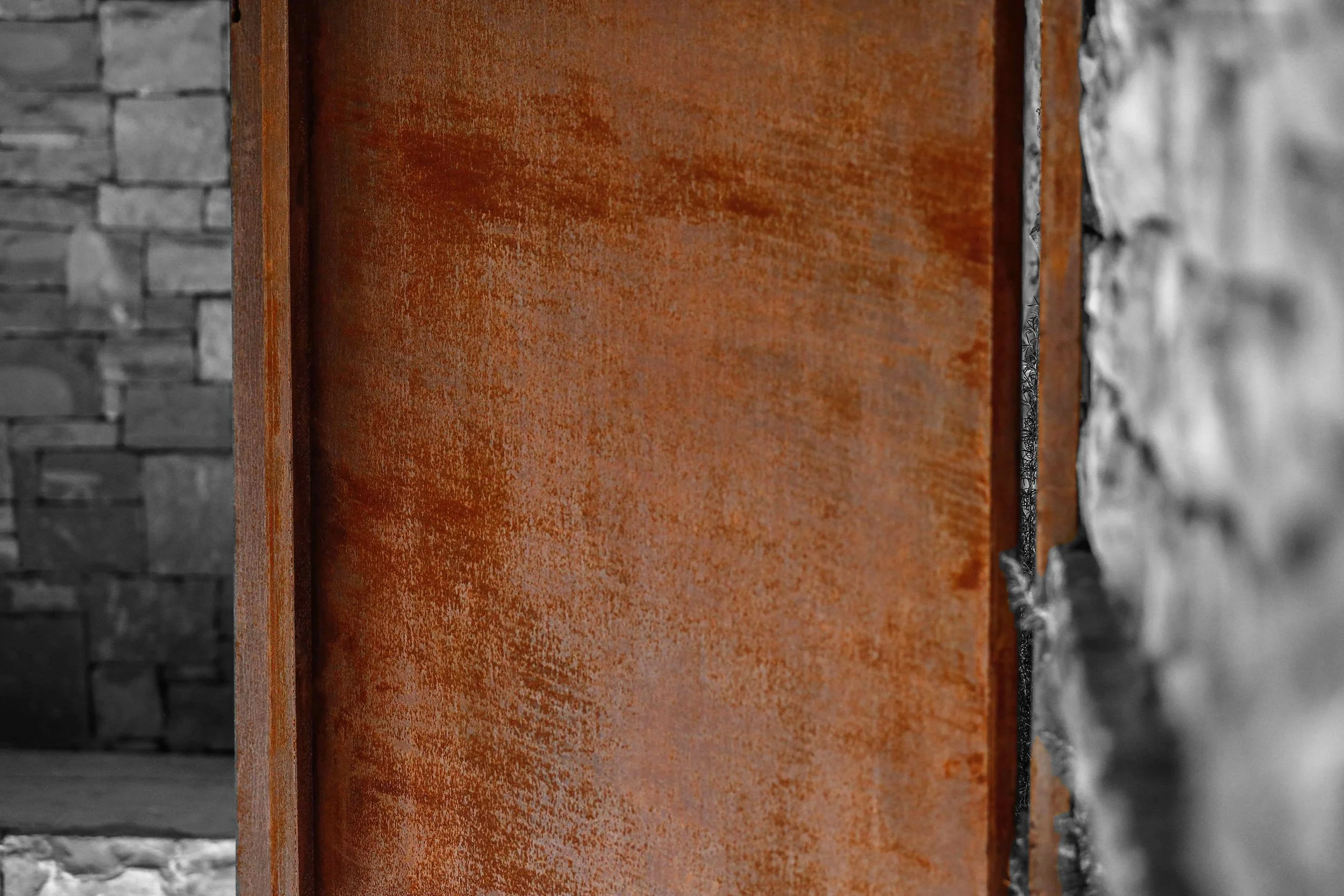Corten steel mature patina — amber surface detail against stone wall